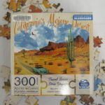 Older blue car driving on highway with cacti and mesas