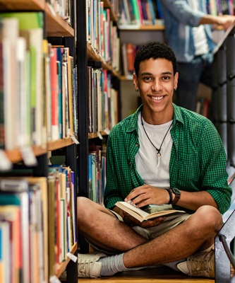 Young man at the Library sitting on the floor with an open book.