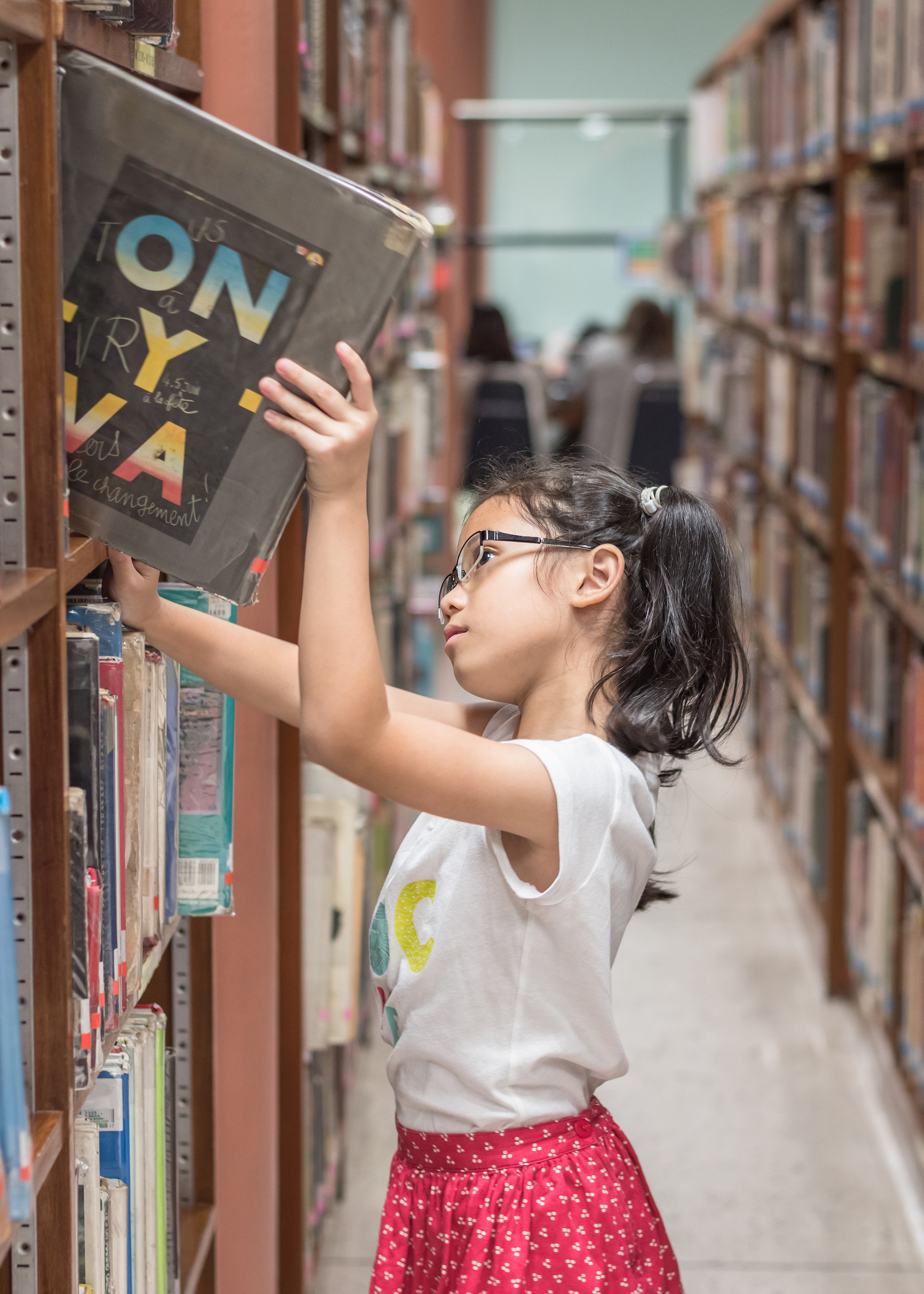 Young girl pulling a library book from the shelves