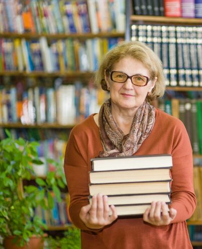 Older adult woman holding a stack of books at the library.