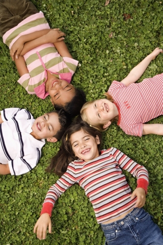 Four kids laying on the grass and laughing.
