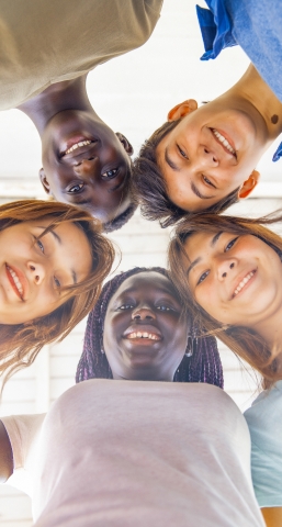 Upward view of teenagers smiling together in a circle. 