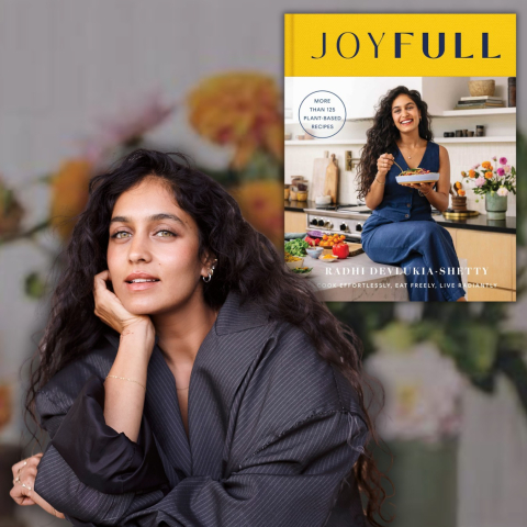 A woman sitting in front of the book Joyfull by Radhi Devlukia-Shetty on a greyed out background with a vase of roses