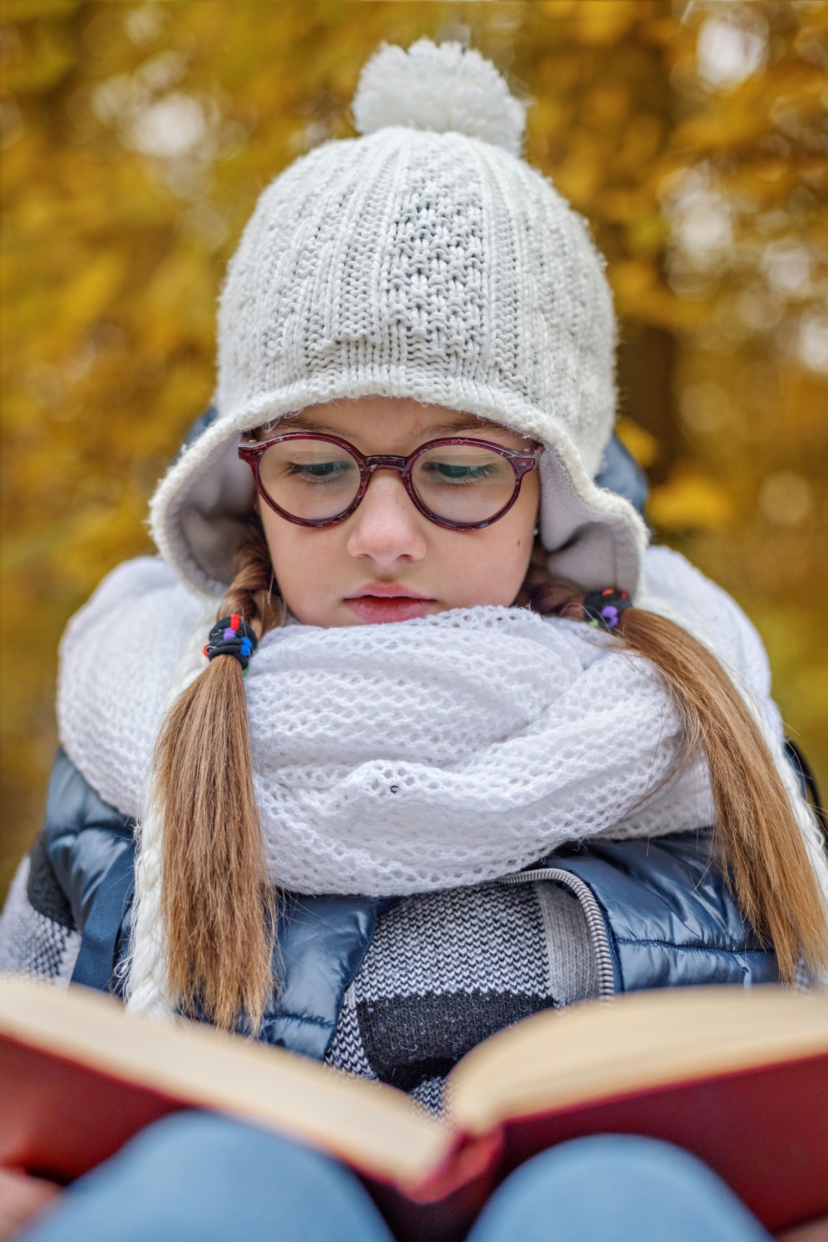 A warmly dressed teen girl reads a book outdoors.