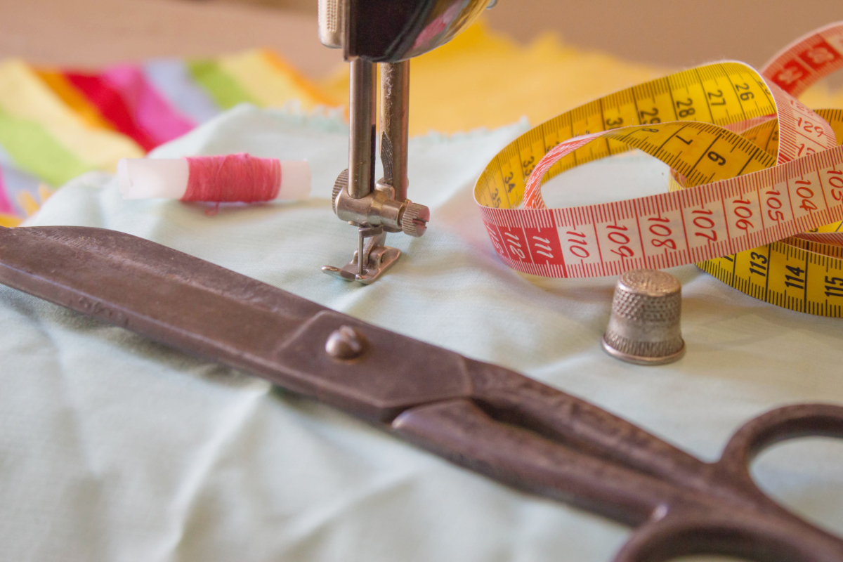 A pair of scissors and a measuring tape sitting next to a presser foot on a sewing machine   