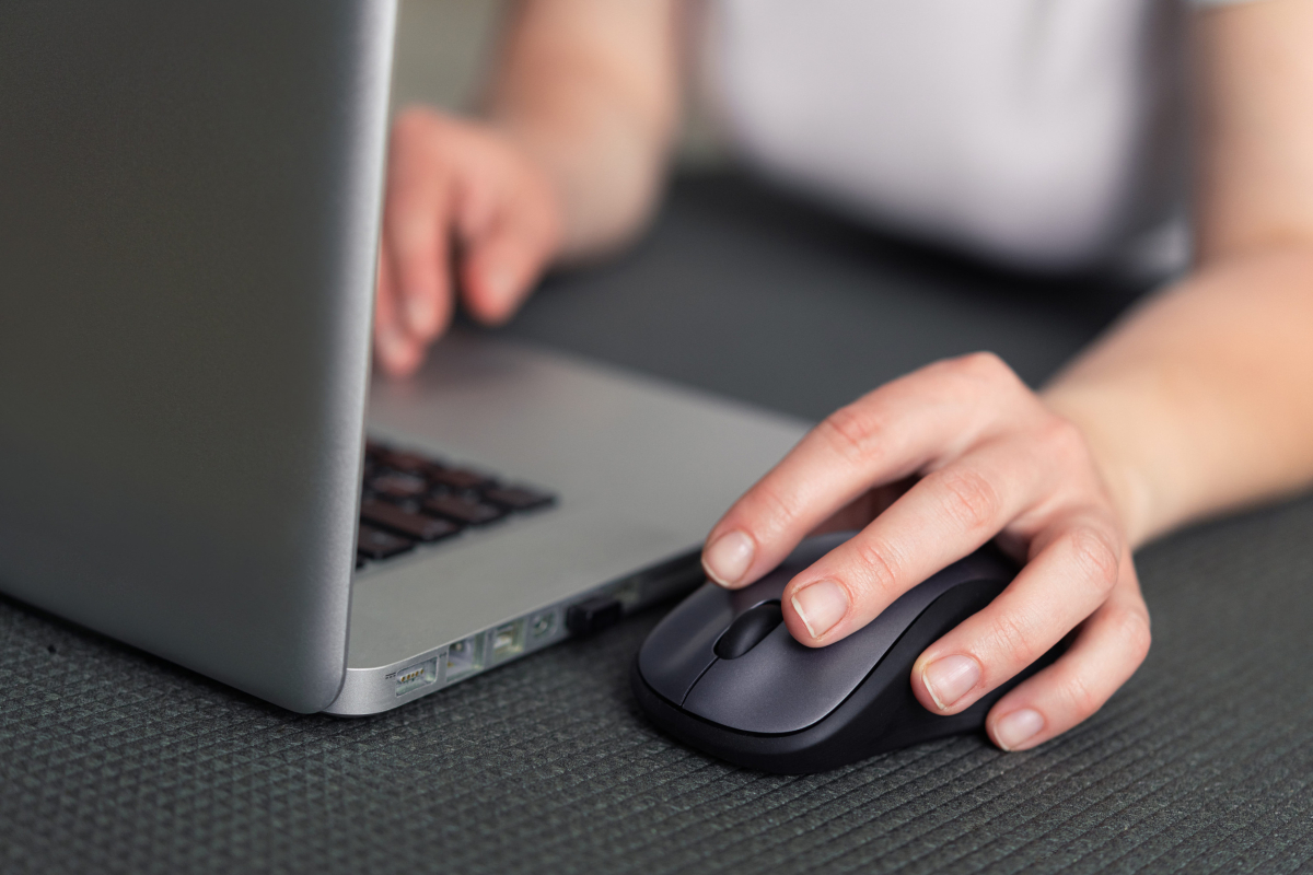 hands holding a mouse and typing on a laptop