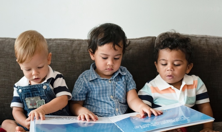 Three adorable Toddler age boys sharing a large picture book.