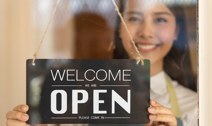 Woman turning OPEN sign in a store window.