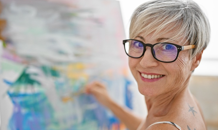 A mature woman smiles as she paints a watercolor picture.